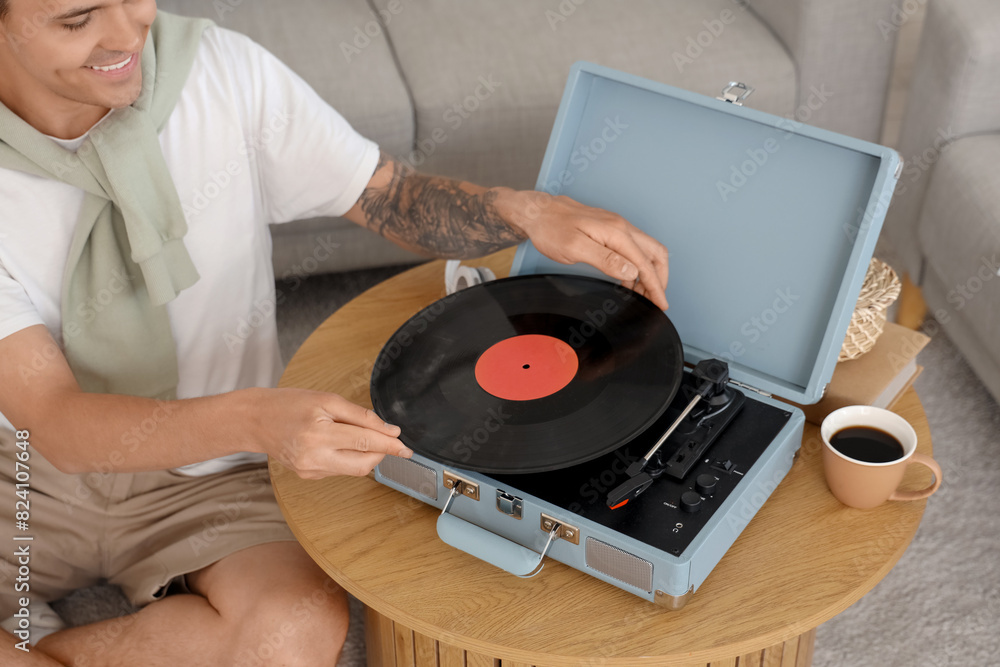 Poster Young man with record player listening to music at home, closeup