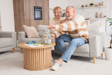 Mature couple putting money in jar at home