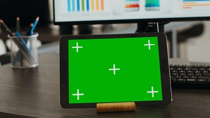 Digital tablet presenting greenscreen display on agency office desk, showing blank chromakey...
