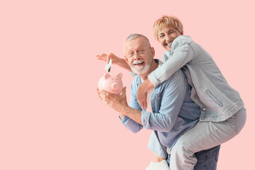 Happy mature couple putting money into piggy bank on pink background