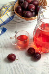 Plum Compote in jug with purple plums on white wooden background. .