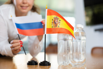 Young woman in business clothes puts flags of Russia and Spain on negotiating table in office