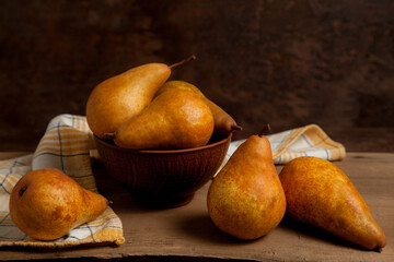 Pears and clay bowl with fruits on wooden background with yellow kitchen towel..