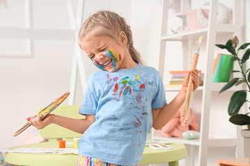 Cute little girl in paint with brushes and palette at home