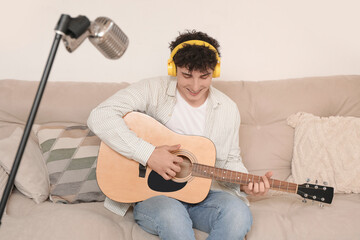 Handsome young man in headphones playing guitar on sofa at home