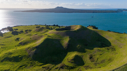 Aerial shot of a grassy volcanic crater on a coastal hillside with the ocean and distant Rangitoto in the background - Musick & Browns Island Motukorea © Rodrigo