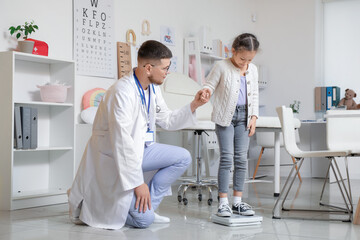 Cute little girl measuring her weight on scales with pediatrician in clinic