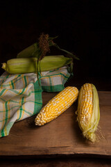 Two cobs sweet corn with green leaves on wooden background..