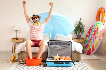 Happy male tourist with basin and suitcase in bedroom on vacation