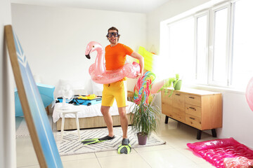 Happy male tourist with snorkeling mask and swim ring in bedroom on vacation