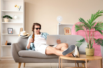 Male tourist with beer using laptop at home on vacation