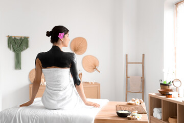 Young woman with mud and flower sitting in spa salon, back view