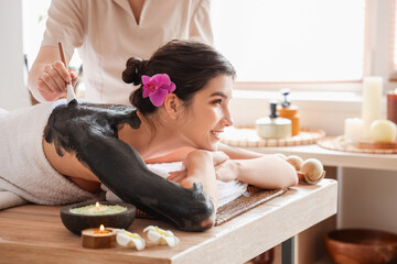 Young woman undergoing mud treatment on table in spa salon