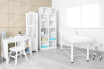 Blurred view of medical office with couch, doctor's workplace and shelf unit