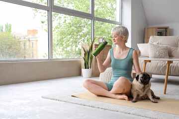Sporty young woman with water bottle and pug dog training at home