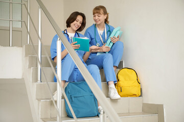 Female medical interns with folders and copybooks sitting on stairs in clinic