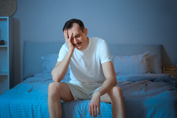 Young man suffering from insomnia in bedroom at night