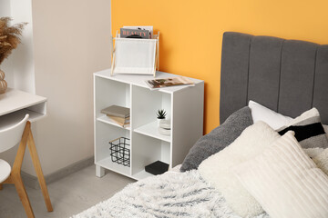 Bedside table with magazines near cozy bed in bedroom