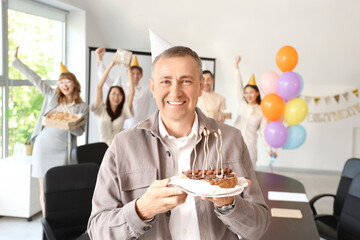 Mature businessman with cake at birthday party in office