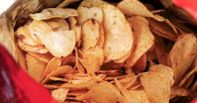 Zoom-in cinematic view of crispy golden potato chips stacked inside a vibrant snack bag