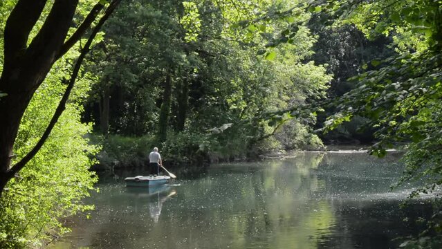 A smoking unrecognizable man quietly punts on a tranquil river surrounded by lush green forest on a sunny day - rear view unrecognizable person cinematic scene