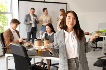Young Asian businesswoman with coffee and sandwich during lunch in office