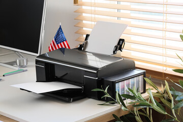 Modern printer with USA flag on desk near window in office
