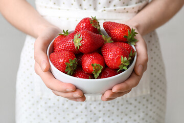 Woman holding bowl with sweet fresh strawberries on grey background, closeup
