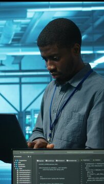 Vertical video Manager in server hub using laptop to find firewall misconfigurations affecting rackmounts performance. Supervisor checking systems bottlenecks leading to sluggish data transfer rates