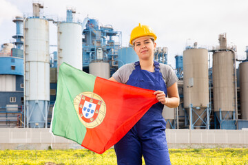 Happy woman waving flag of Portugal against the background of a modern factory