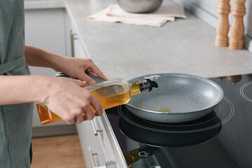 Vegetable fats. Woman pouring cooking oil into frying pan on stove in kitchen, closeup