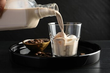 Pouring coffee cream liqueur into glass at black wooden table, closeup