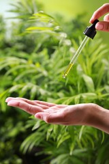 Woman dripping essential oil from pipette outdoors, closeup
