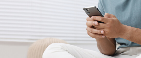 Man typing message on mobile phone indoors, closeup. Banner design with space for text