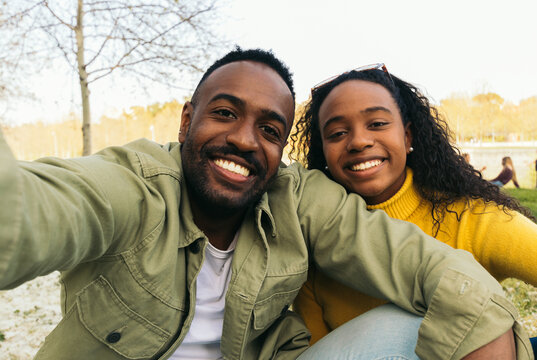 afro american couple taking a selfie sitting in a park - Powered by Adobe