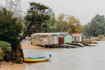 Obraz premium A row of colorful beach huts lined up neatly next to the waters edge on a sunny day. The huts are uniquely designed and each painted in different vibrant colors, creating a striking, picturesque scene