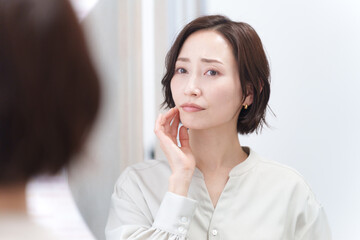 鏡を見て肌荒れに悩むミドル女性（美容・スキンケア・肌トラブル）