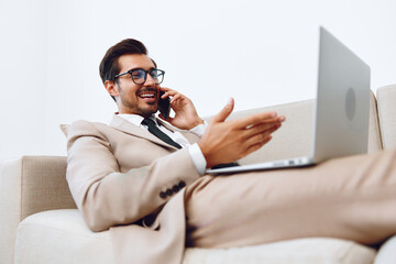 Male businessman lying on couch with laptop and talking on phone, video call online technology in business and data analytics, good deal, lifestyle manager.