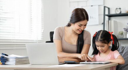 Asian mom helping her little daughter doing homework while working from home