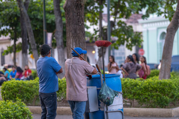 Municipal city cleaner in the city center main square park with a broom and large garbage bin....