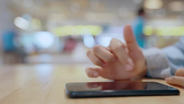 A person is using a cell phone to touch a screen. The phone is on a wooden table