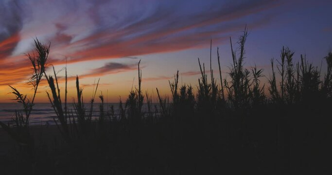 Playa de El Palmar beach at sunset on Spanish coastline with people walking and calm waves with orage purple sky