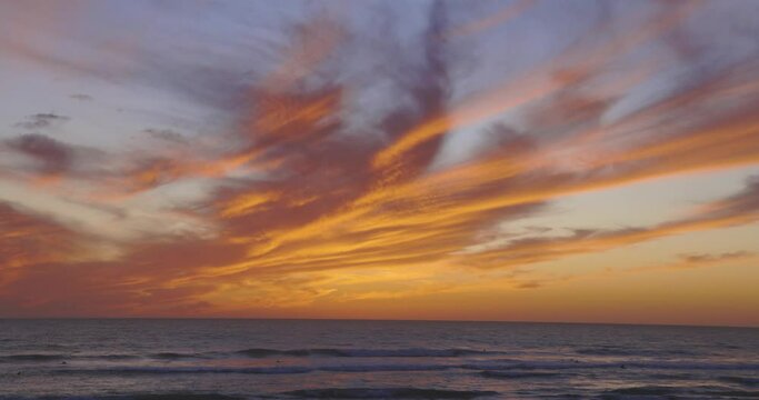 People surfing and swimming at sunset in ocean with calm waves at dramatic sunset with orange and purple sky