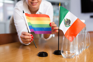Preparing for business negotiations - woman sets small flags of countries of Mexico and LGBT on the...