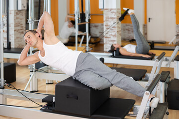 Man with help of informer is engaged in Pilates studio and performs exercises to strengthen muscles...