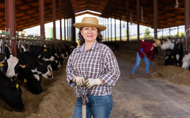 Portrait of mature positive woman farmer working in cowshed at dairy farm © JackF