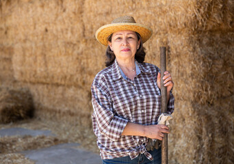 Portrait of an elderly confident woman farmer, standing near the haystacks, holding a pitchfork in her hand. Close-up ..portrait