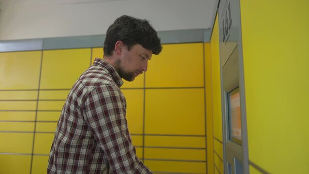 Yellow self-service postal terminal. Man sending parcel. Parcel pick up point, contactless self service post terminal, parcel delivery. Man putting box to parcel machine. Deposit for package storage