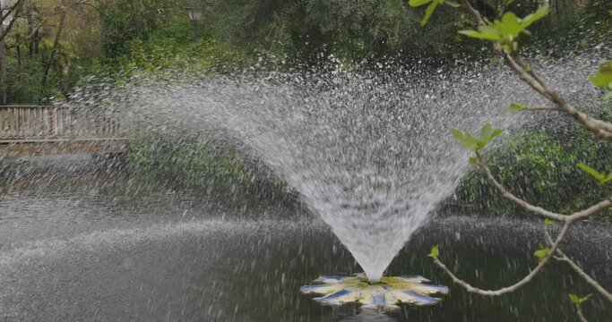 Water fountain splashing in Maria Luisa park in Seville on a cloudyday with green vegetation and trees