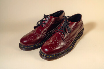 Close up of maroon wingtip brogue shoes with rubber outsole made from genuine cow leather. Studio shot of an elegant and shiny vintage shoe product on a beige background
